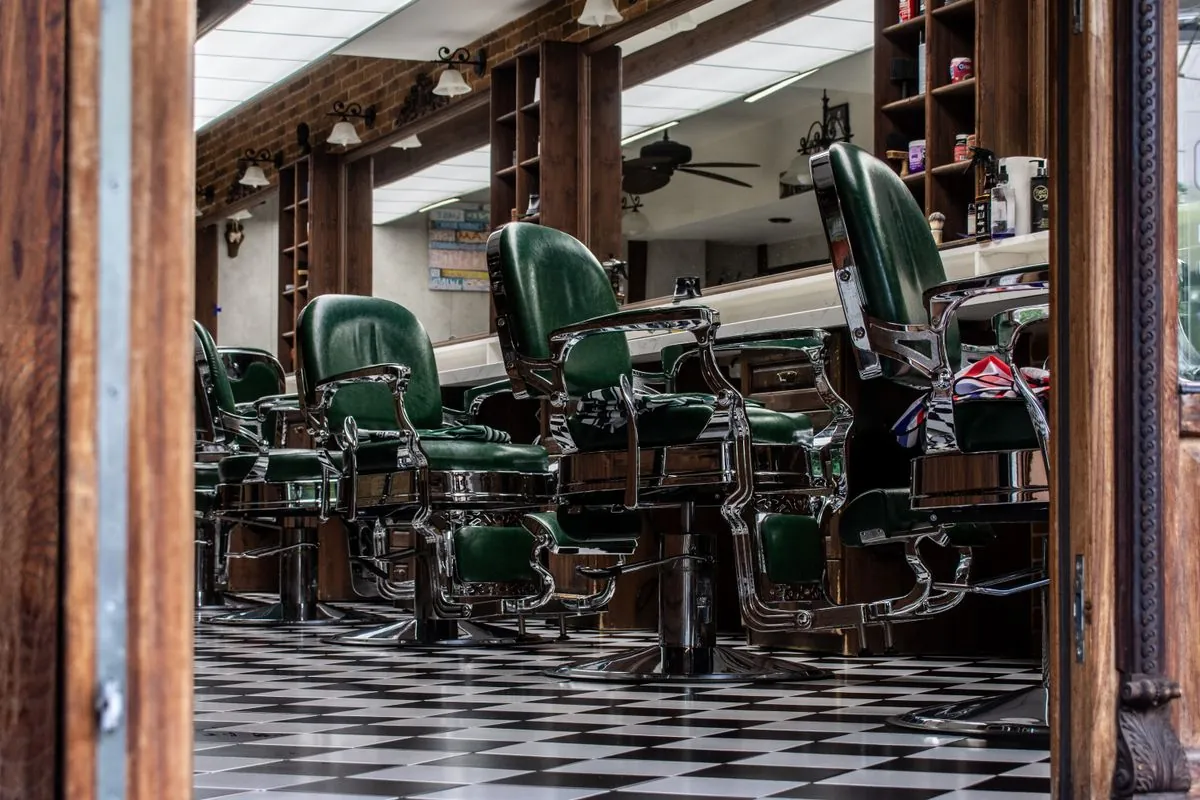 A row of green leather barber chairs in a dark wood shop