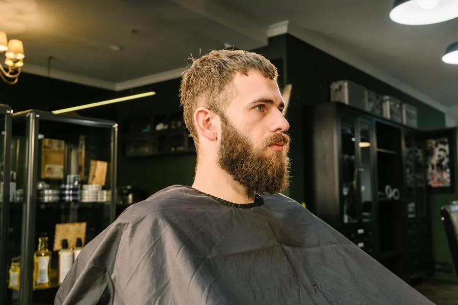 A barber in a dark cape mid-cut, seen in profile